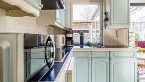 A kitchen with teal cabinets, a coffee maker, and a window overlooking a wooden deck. - Amazing Holiday Home in Lauwersoog With Sauna (Lauwersoog)
