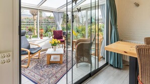 A sunlit room with a glass door leading to a garden, featuring a wooden table, wicker chairs, and a patterned rug. - Amazing Holiday Home in Lauwersoog With Sauna (Lauwersoog)