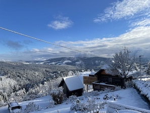A cabin with a snow-covered roof, surrounded by a snowy landscape and a clear blue sky.