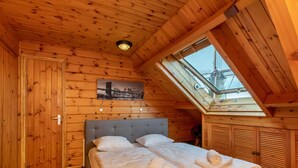 Quarto de cabana de madeira com cama, um claraboia e uma fotografia da paisagem urbana na parede.