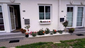 A building with numbered windows, a flower bed, and a paved walkway. - Fillner 2 Modern Retreat (Scharbeutz)
