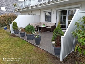 Una terraza con mobiliario exterior, plantas en macetas y una cerca blanca.