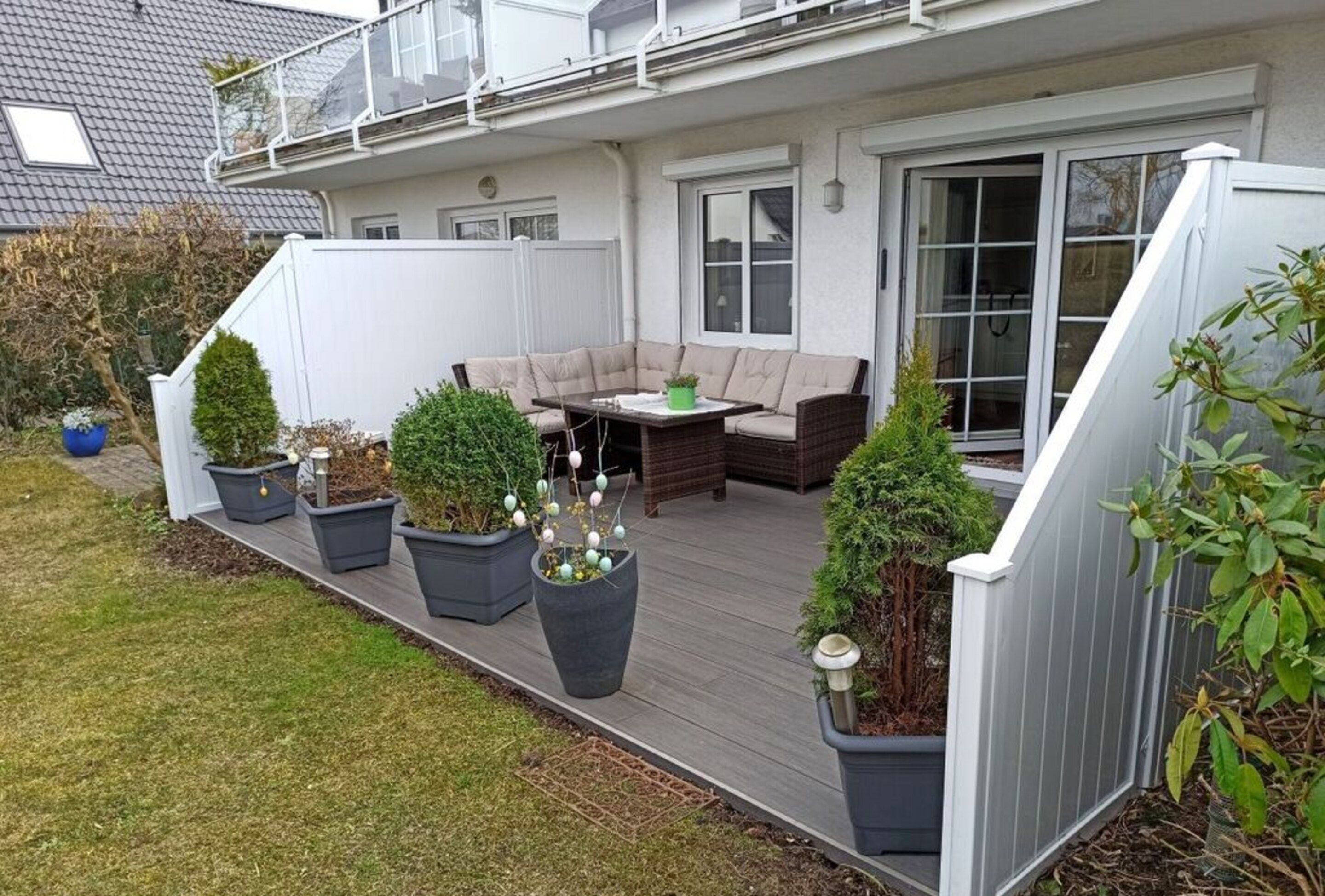 A deck with outdoor furniture, potted plants, and a white fence.