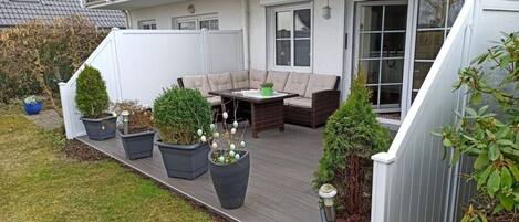 A deck with outdoor furniture, potted plants, and a white fence.