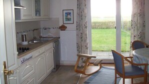 A kitchen with white cabinets, a sink, and a dining area with a table and chairs. - Pellworm in Haus Halligblick (Dagebuell)