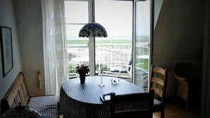 A dining area with a table and chairs, a hanging lamp, and a view of a green landscape through a large window. - Pellworm in Haus Halligblick (Dagebuell)