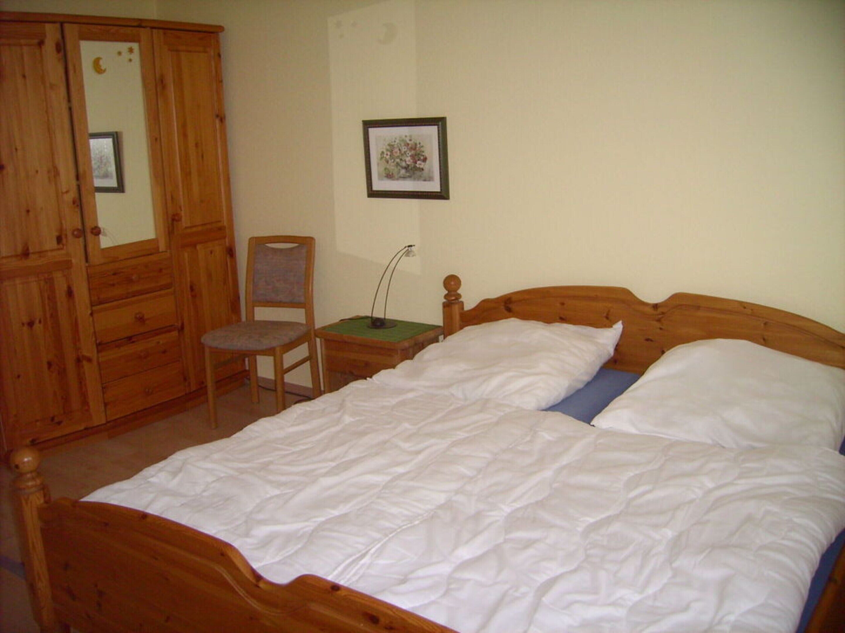 Een slaapkamer met een houten bed, een stoel, een bureau en een kledingkast.