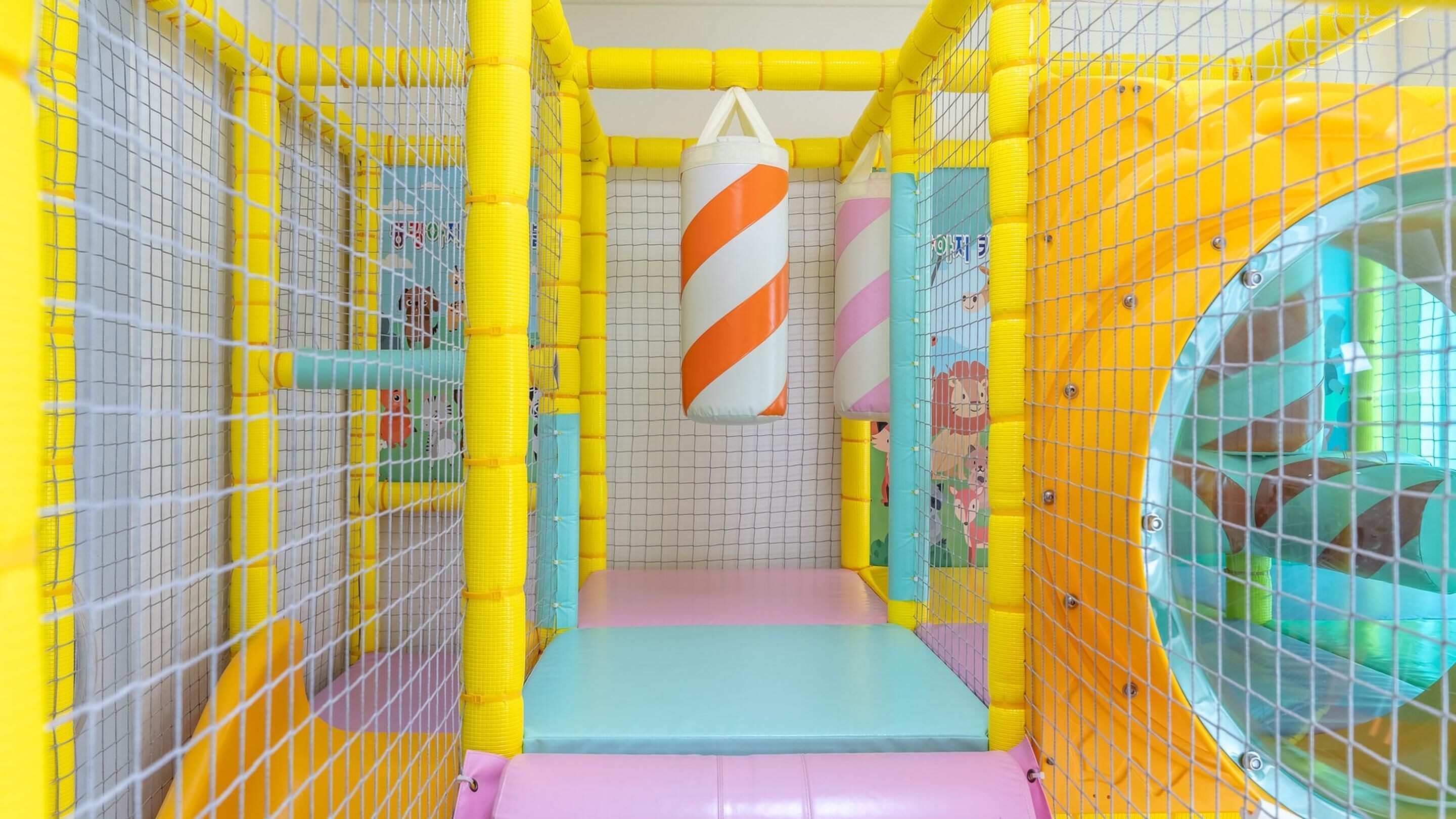 Un espace de jeux intérieur aux couleurs vives, doté d’un sol rembourré, de murs jaunes et bleus, et d’un sac de frappe.