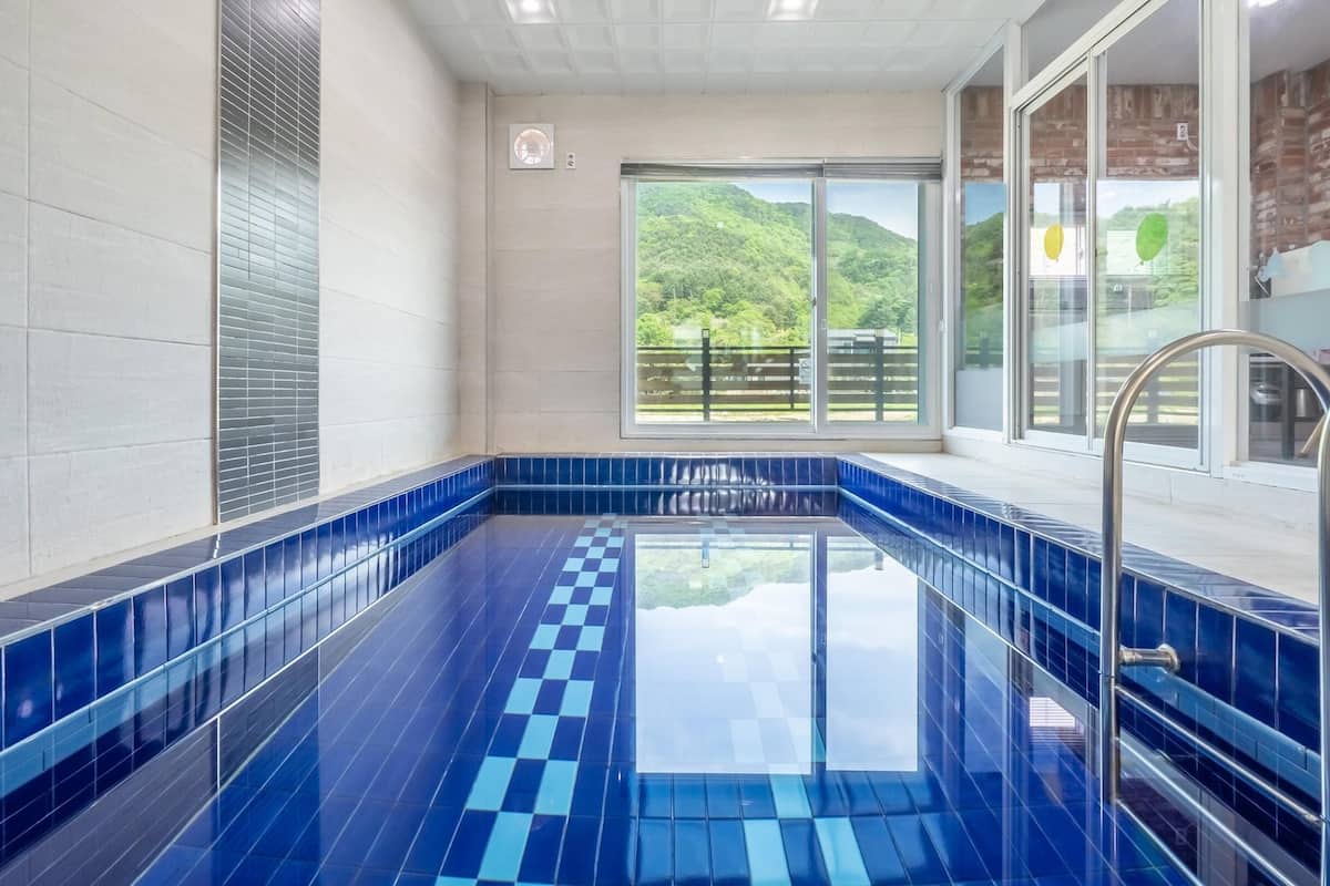 Une piscine aux carreaux bleus, une porte vitrée donnant sur l’extérieur et une vue sur la verdure.