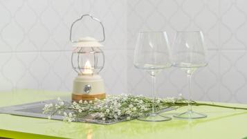 A table with two clear wine glasses, a lit lantern, and a sprig of white flowers on a green surface.