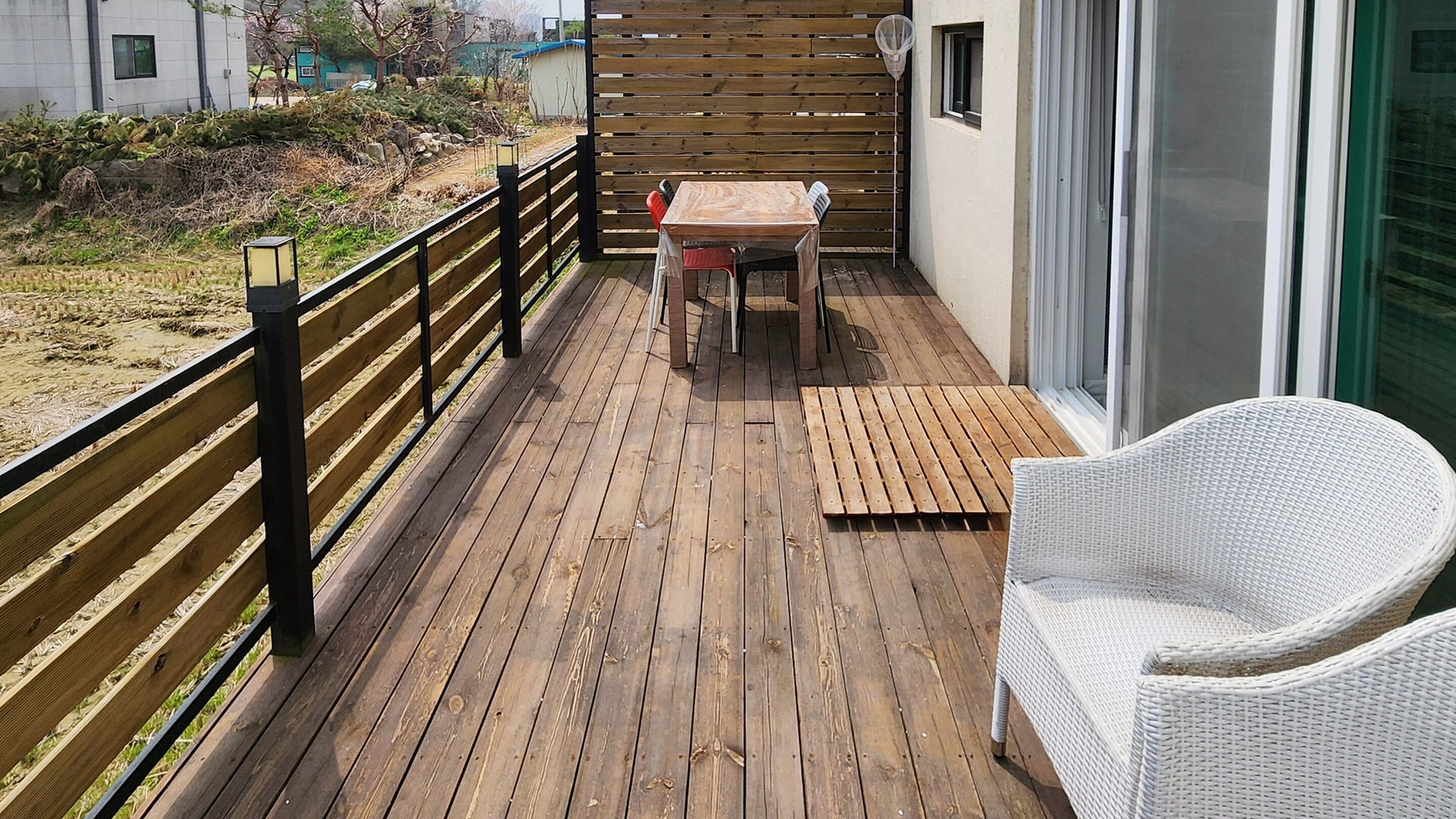 A wooden deck with a table and chairs, a wicker chair, and a view of the surrounding area.