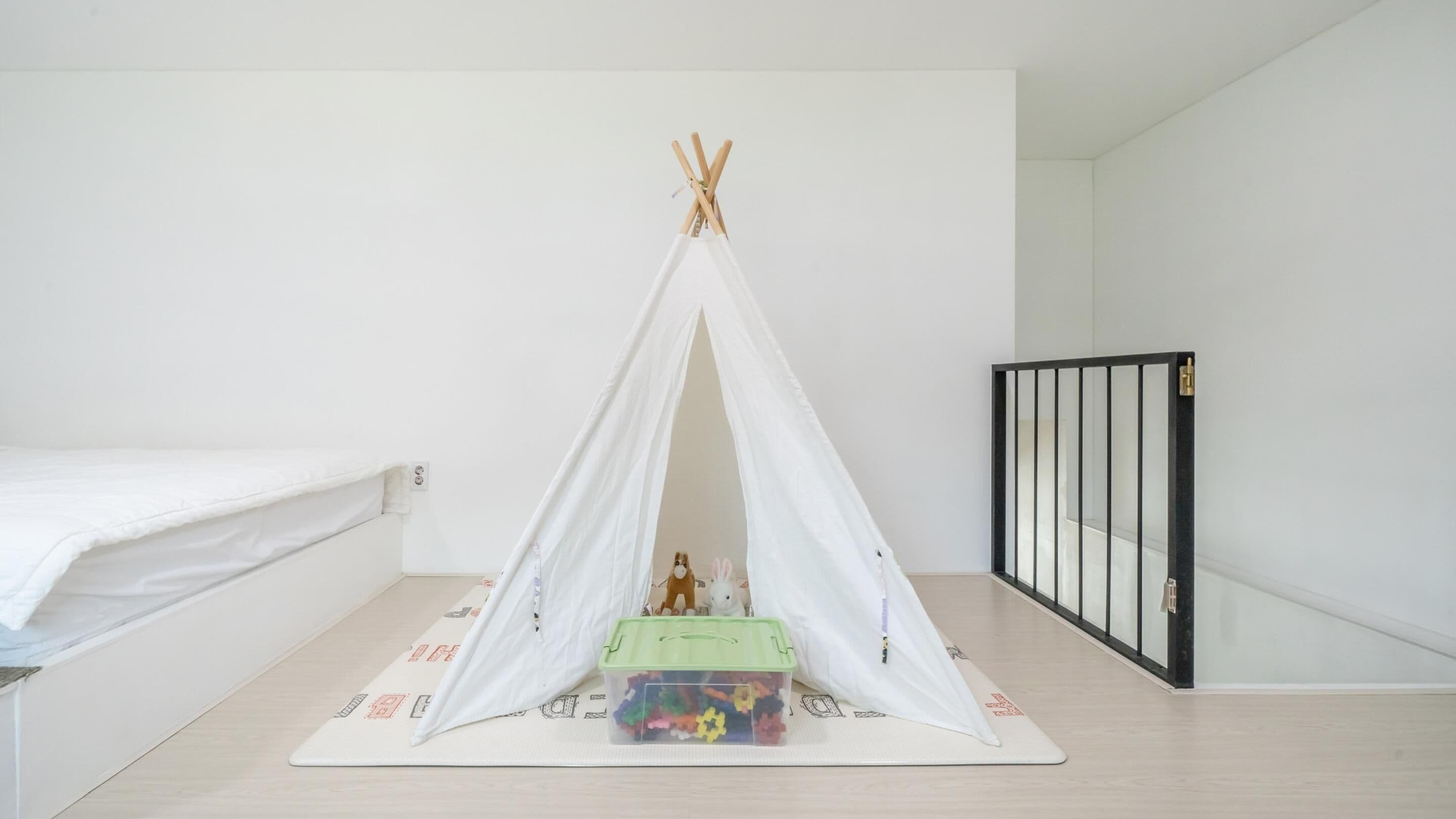 A room with a white bed, a white tent-like structure, and a play area with toys and a green container.