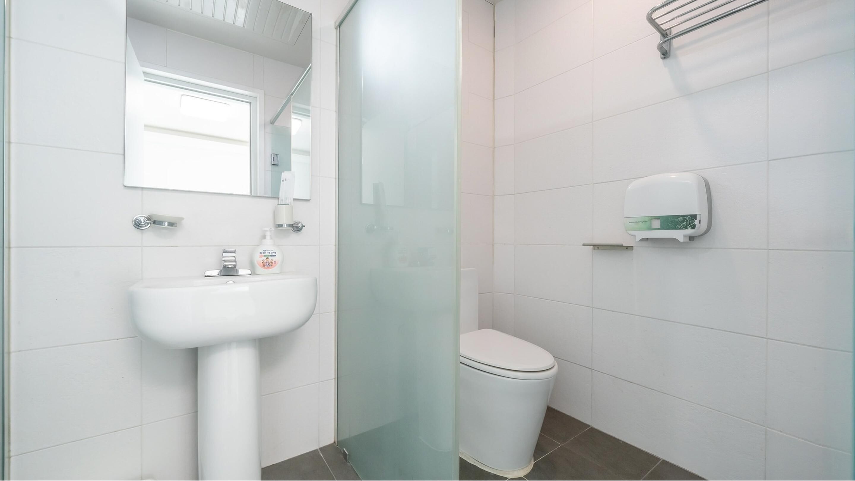Une salle de bain avec un lavabo blanc, des toilettes et un distributeur de gel hydroalcoolique fixé au mur.