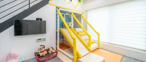 Un área de juegos con un tobogán, una red de escalada y un caballo balancín.