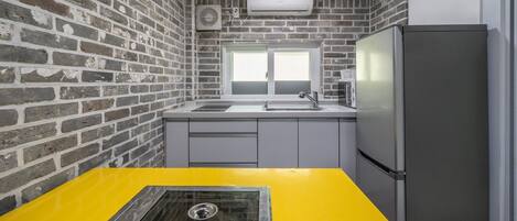 Eine kleine Küche mit Backsteinwand, gelber Arbeitsplatte, einem Edelstahlkühlschrank und einem Fenster über der Spüle.