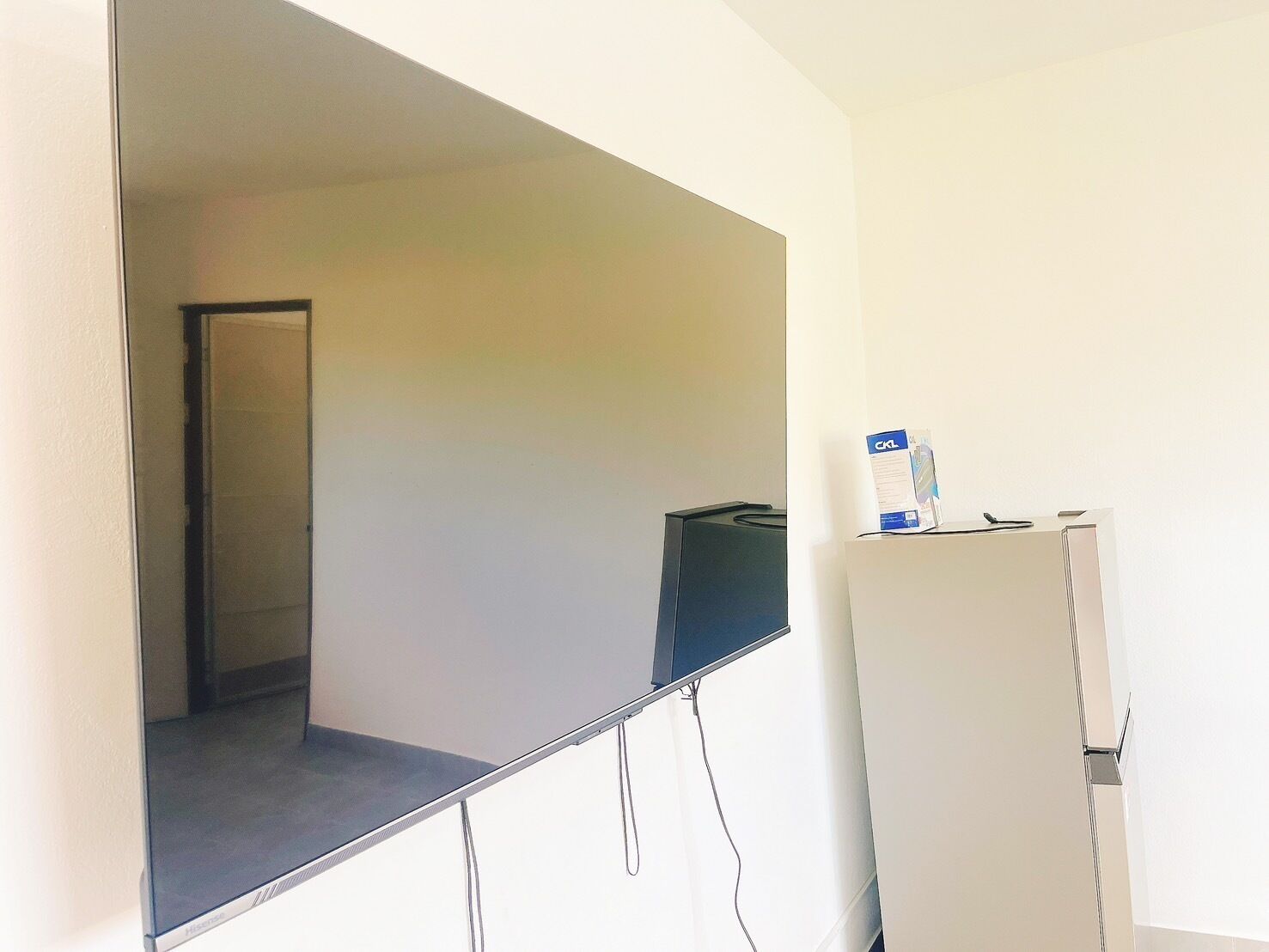 A room with a large flat-screen TV mounted on the wall, a white refrigerator, and a door leading to another room.