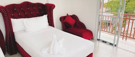 A hotel room with a red upholstered bed, white bedding, and a red armchair.