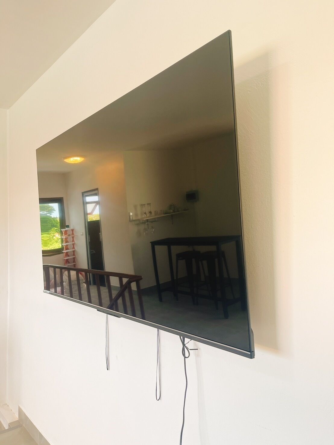 A flat-screen TV mounted on a wall with a visible dining area in the reflection.