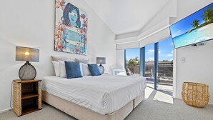 Un dormitorio moderno con una cama grande, dos lámparas de noche, un ventanal con vista a la playa y una cesta tejida en el suelo.