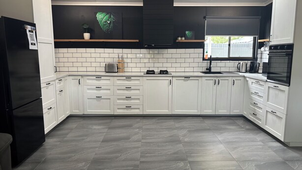 Een moderne keuken met witte kasten, een zwarte koelkast en een betegelde achterwand.