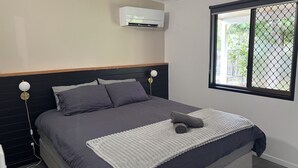 Een net opgemaakt bed met donkere lakens, een witte deken en een opgerolde handdoek.