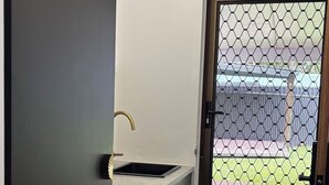 Een kleine keuken met een wasmachine, een spoelbak en een deur naar een buitenruimte met een omheining.