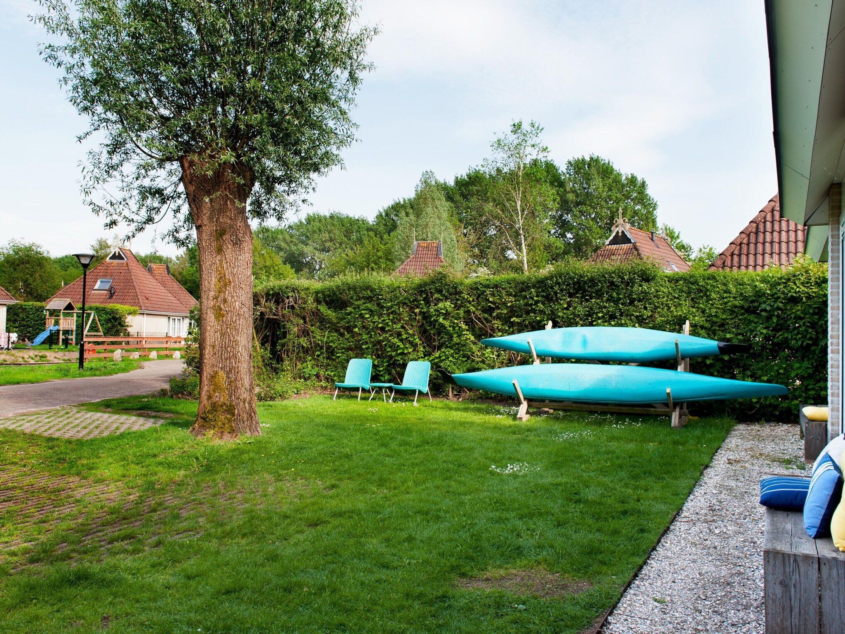 Une cour verdoyante avec un arbre, deux kayaks bleus et un banc.