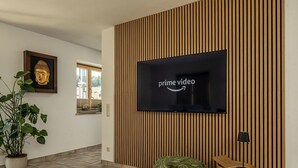 A modern living room with a large flat-screen TV mounted on a wooden panel wall, a Buddha statue, and a potted plant. - Ferienwohnung Marianne Bergpanorama (Berchtesgaden)