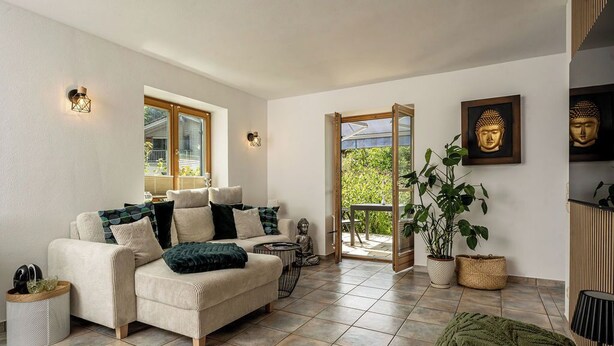 A modern living room with a sofa, a Buddha statue, and a large window. - Ferienwohnung Marianne Bergpanorama (Berchtesgaden)