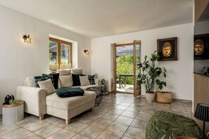 A modern living room with a sofa, a Buddha statue, and a large window. - Ferienwohnung Marianne Bergpanorama (Berchtesgaden)