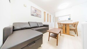 A modern living room with a grey sofa, a wooden dining table, and a kitchen area in the background. - Tokyo Private House (tokyo)