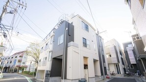 A modern multi-story residential building with a garage entrance, visible electrical infrastructure, and bicycles parked outside. - Tokyo Private House (tokyo)