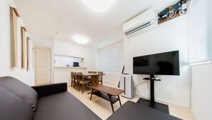 A modern living room with a sofa, a dining table with chairs, a flat-screen TV, and an air conditioning unit mounted on the wall. - Tokyo Private House (tokyo)