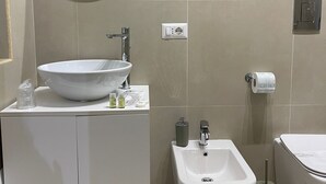 Une salle de bain moderne avec un grand miroir rond, un lavabo blanc, un bidet et des toilettes.
