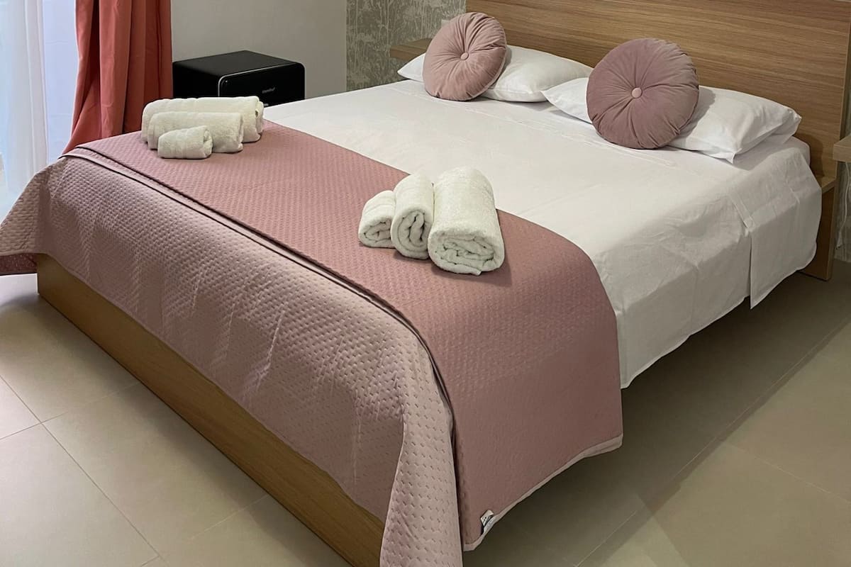 A neatly made bed with pink bedding, two pillows, and rolled towels.