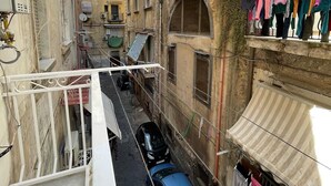 Une rue étroite en milieu urbain, bordée de bâtiments des deux côtés, avec une voiture bleue garée dans la rue et des vêtements suspendus à un fil à linge devant un immeuble.