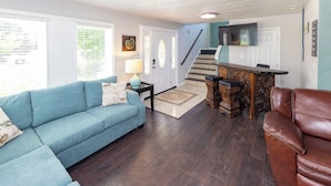 Ein Wohnzimmer mit einem blauen Sofa, einem braunen Ledersessel, einem Holztisch, einer Treppe und einem an der Wand befestigten Fernseher.