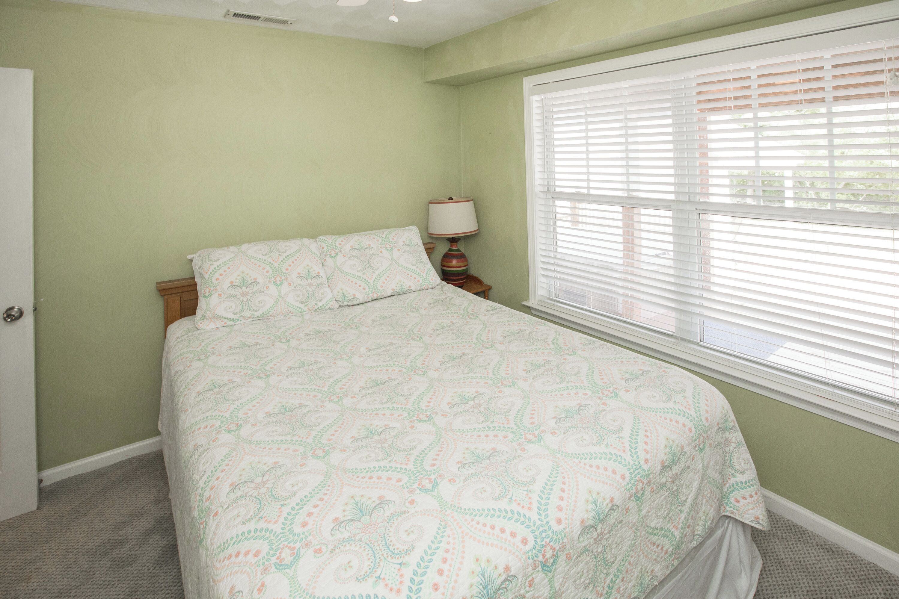 A bedroom with a bed, a nightstand, a lamp, and a window with blinds.