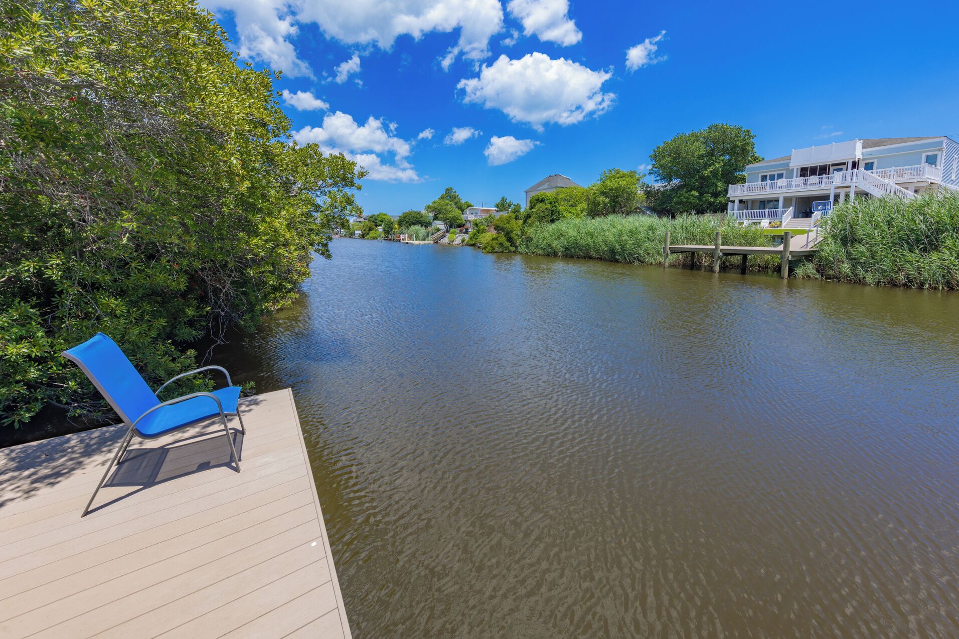 A riverside deck with a blue chair, a wooden walkway, and a building with a balcony in the background.