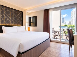 A hotel room with a large bed, a view of the city, and a balcony with chairs.