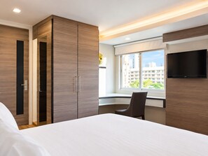 A hotel room with a bed, a desk, a chair, a TV, and a wardrobe.