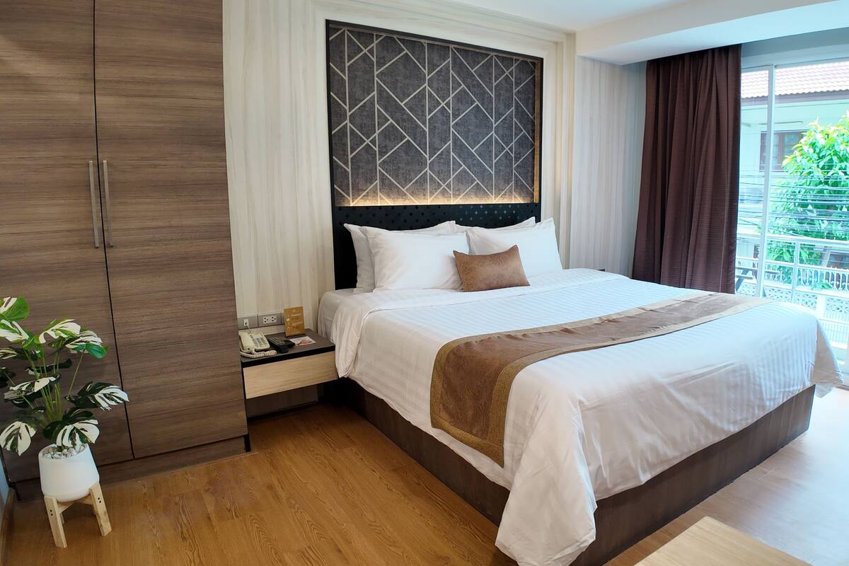 Een hotelkamer met een groot bed, een nachtkastje, een telefoon, een kamerplant en uitzicht op het buiten.