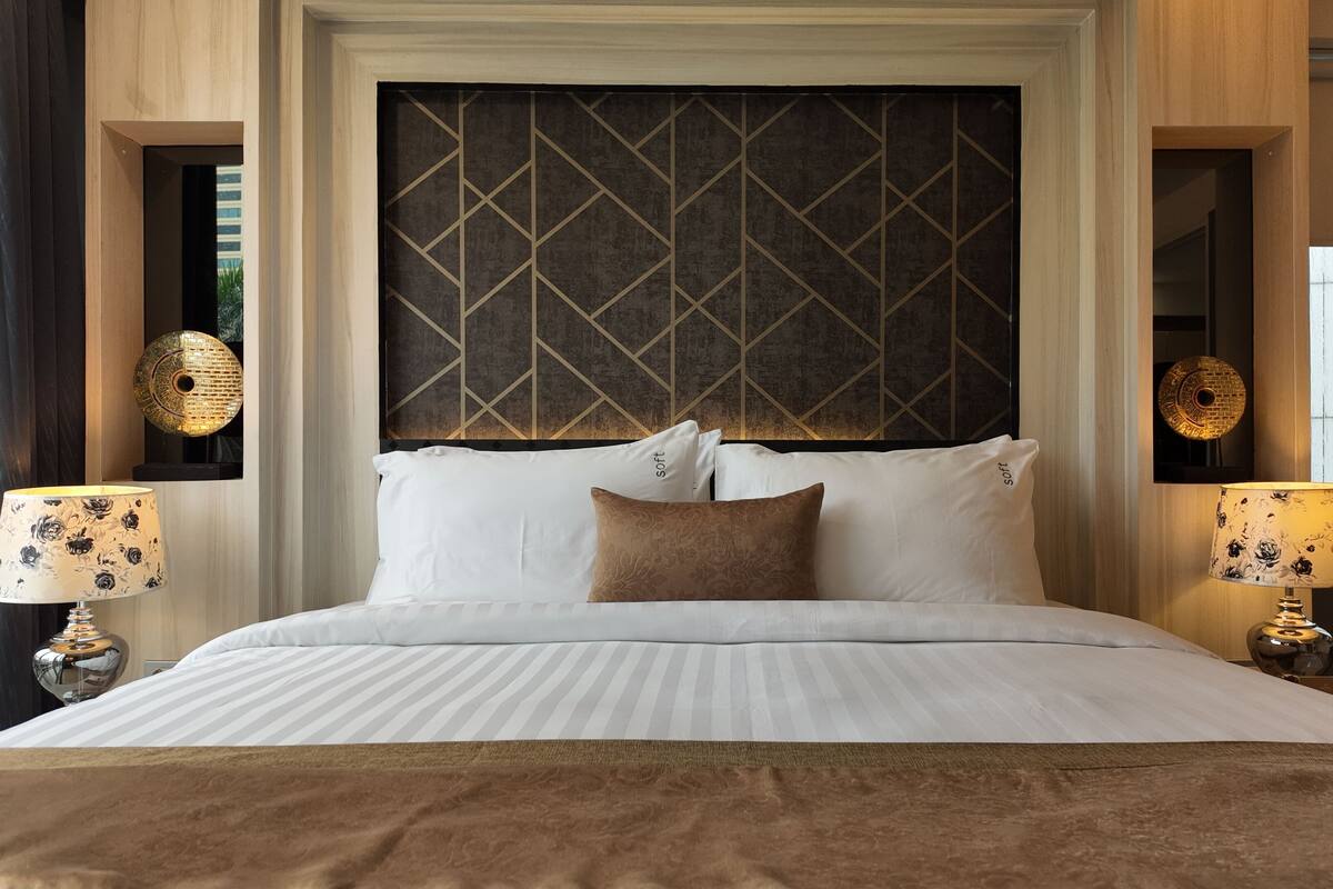 Een hotelkamer met een groot bed, twee bedlampen, een decoratief hoofdbord en uitzicht op buiten.