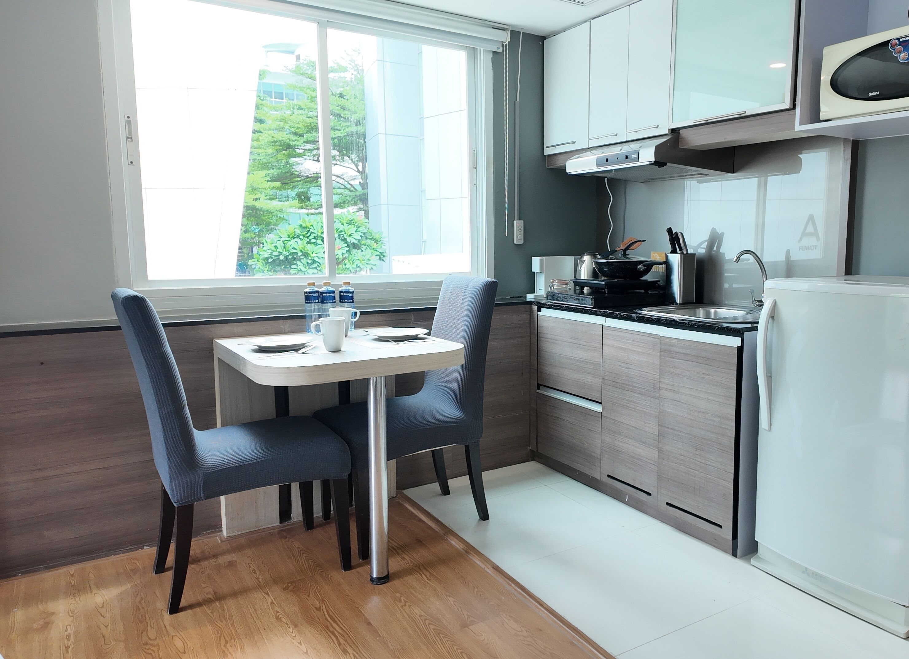 A compact kitchen with a dining table and chairs, a microwave, and a refrigerator.