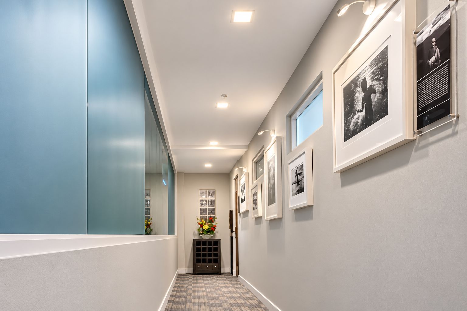 A hallway with framed pictures on the wall, a small window, and a door at the end.