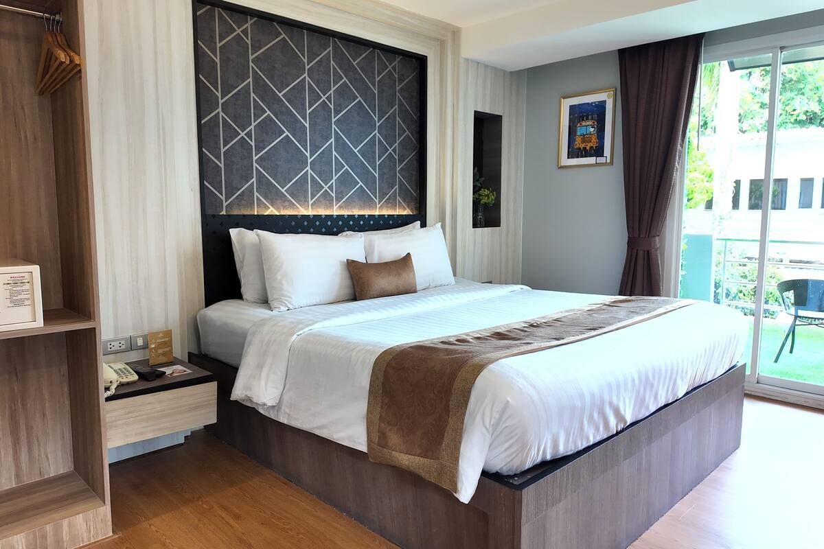 Een hotelkamer met een groot bed, een nachtkastje met een telefoon en een kaart, een garderobe en uitzicht op buiten.