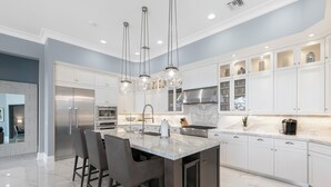 A modern kitchen with a central island, stainless steel appliances, and white cabinetry. - Relax with Pool, Hot Tub, Fire Pit & Waterfront Views (Marco Island)