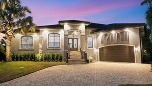 A two-story house with a driveway, a garage, and a well-maintained lawn. - Relax with Pool, Hot Tub, Fire Pit & Waterfront Views (Marco Island)
