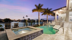A swimming pool with a jacuzzi, palm trees, and a view of the city at dusk. - Relax with Pool, Hot Tub, Fire Pit & Waterfront Views (Marco Island)