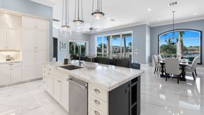 A modern kitchen with a marble island, white cabinetry, and pendant lighting. - Relax with Pool, Hot Tub, Fire Pit & Waterfront Views (Marco Island)